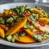 A close-up of the glossy, citrusy salad shows juicy mango strips glistening in a tangy lime-honey vinaigrette. The red onion and cilantro flecks create a beautiful contrast for a light, gluten-free dinner side.  