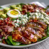 Colorful Cobb Salad Bowl topped with quartered eggs, diced tomatoes, and ranch dressing served in a rustic bowl.