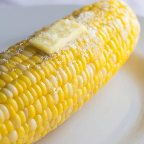 Grilled corn on the cob, slightly charred, offering a smoky flavor, ready for summer.