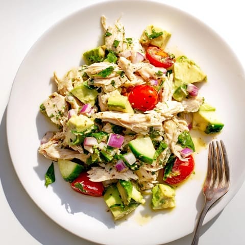 A close-up of homemade avocado chicken salad on a rustic wooden table, garnished with cilantro and a squeeze of zesty lime.