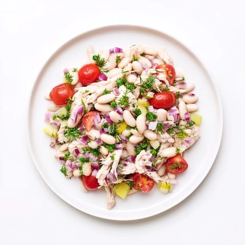 A close-up of Lemony White Bean Chicken Salad featuring juicy cherry tomatoes, red onion, parsley, and glistening olive oil-lemon dressing on fluffy cannellini beans.  