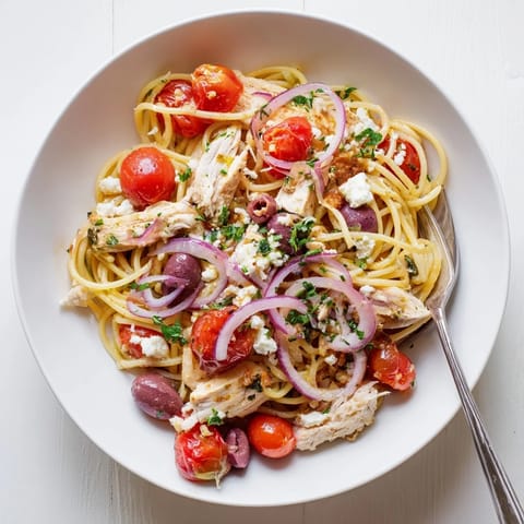 A close-up of Greek Chicken Spaghetti topped with crumbled feta and fresh parsley beside a glass of wine.
