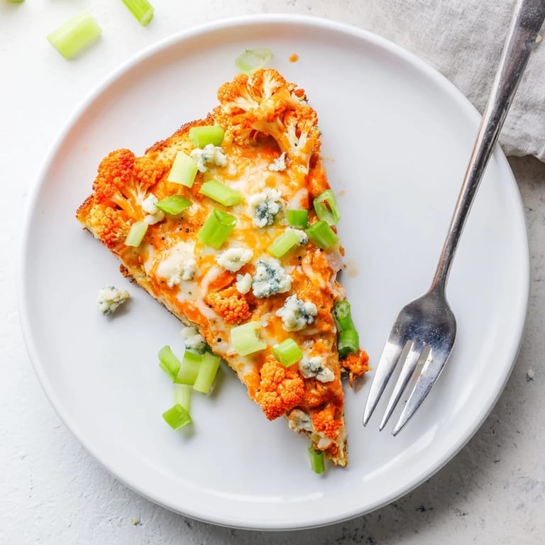 A close-up view of a vegetarian Buffalo Cauliflower Pizza with a crispy crust and drizzled buffalo sauce on a marble board.