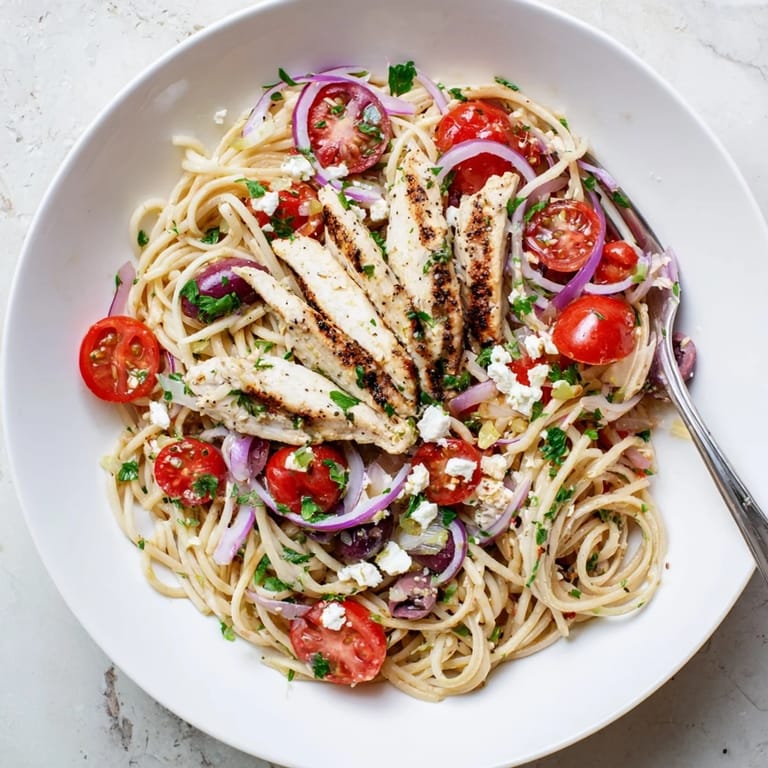 Warm Greek Chicken Spaghetti served on a rustic plate with sliced chicken, red onion, and Kalamata olives.